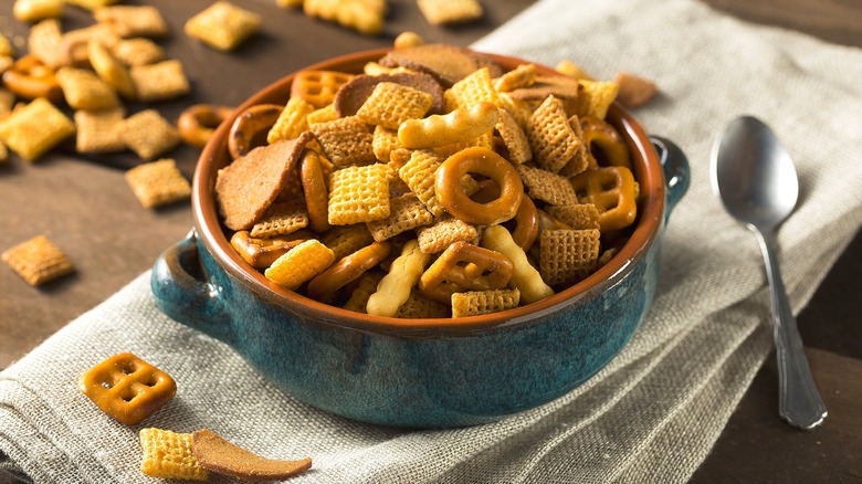 Chex mix in a blue and brown ceramic bowl with handles over a folded cloth napkin