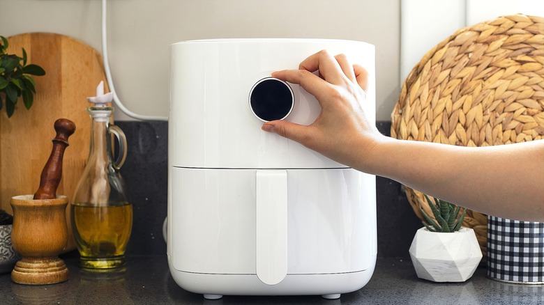 A hand turning a black control knob on a white air fryer