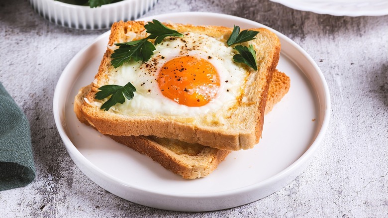 Two pieces of fried eggs in toast topped with fresh parsley on a white plate