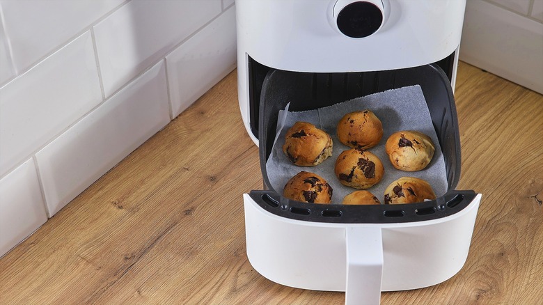 Puffy chocolate chip cookies on a piece of parchment paper in an open air fryer on a wooden countertop
