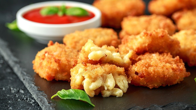 Close-up of fried macaroni and cheese bites with fresh basil and marinara sauce on a black serving board