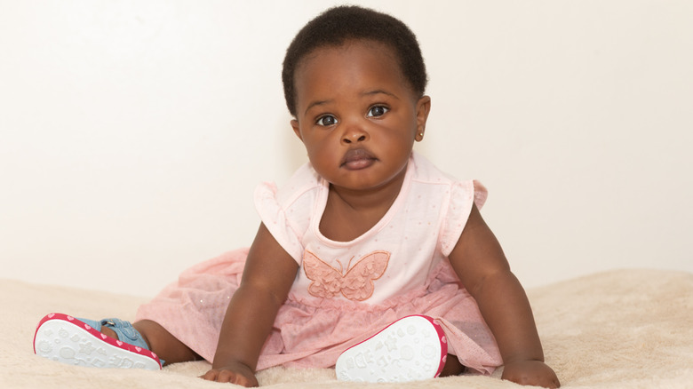 Black baby girl in pink dress sitting on bed