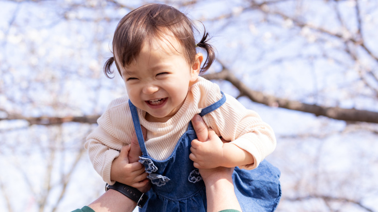 Smiling baby girl being lifted up outdoors