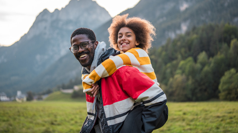 Man giving daughter piggyback ride with mountain background