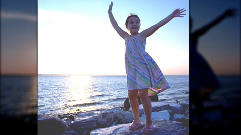 Girl in striped dress on rocks by water