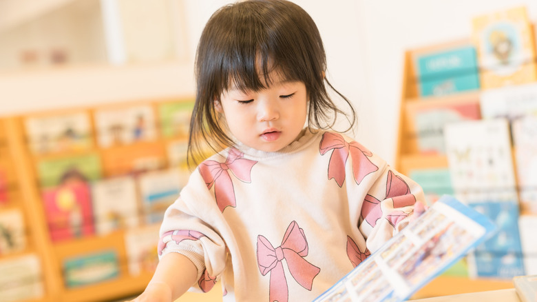 Toddler girl looking at book wearing a sweater with pink ribbons