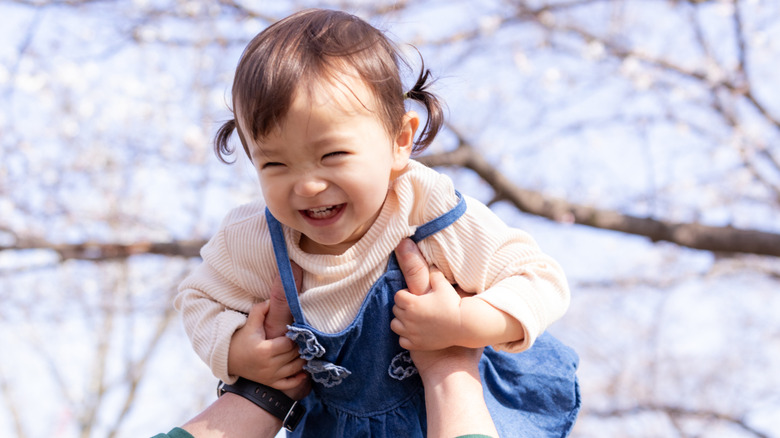Baby smiling while a parent holds her up
