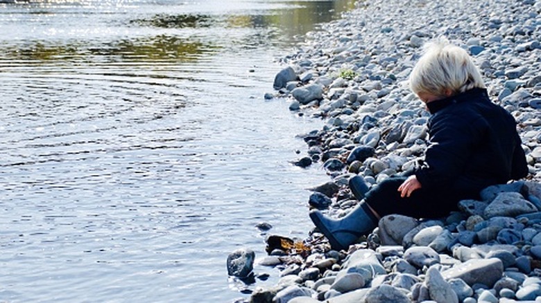 Toddler boy in boots and coat looking at stream