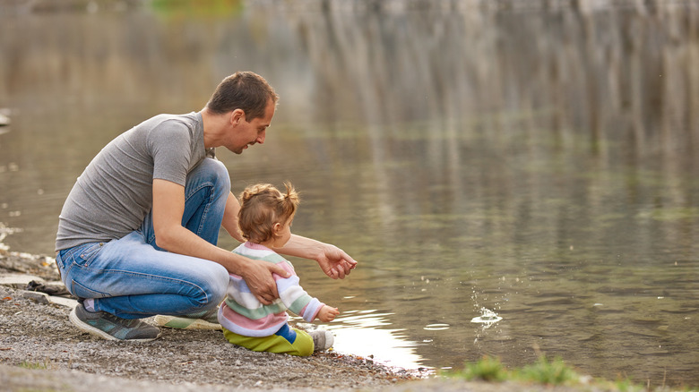 Toddler girl at water's edge with dad