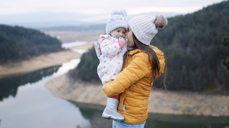 mom holding bundled up little girl in front of a river