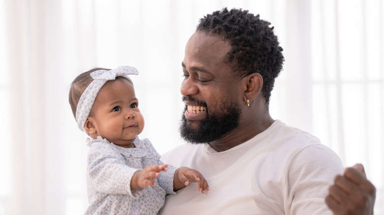 A baby girl is held by her father as he smiles at her