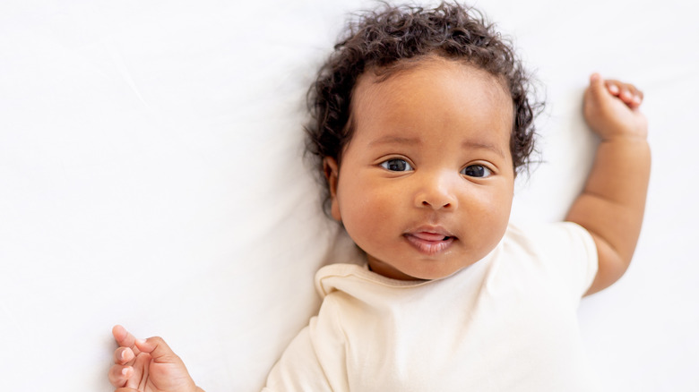 A baby lies on a bed looking at the camera