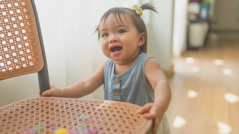 Toddler girl with little pigtails standing up holding onto a chair