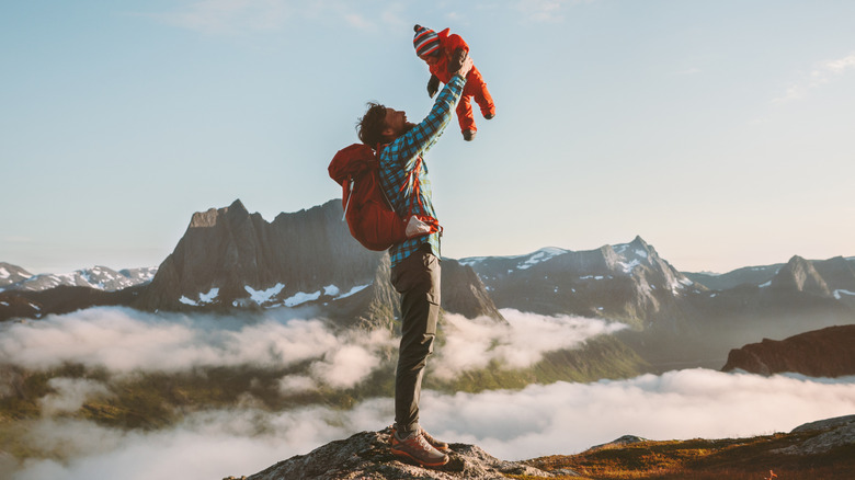 Parent holding baby in air in front of mountain