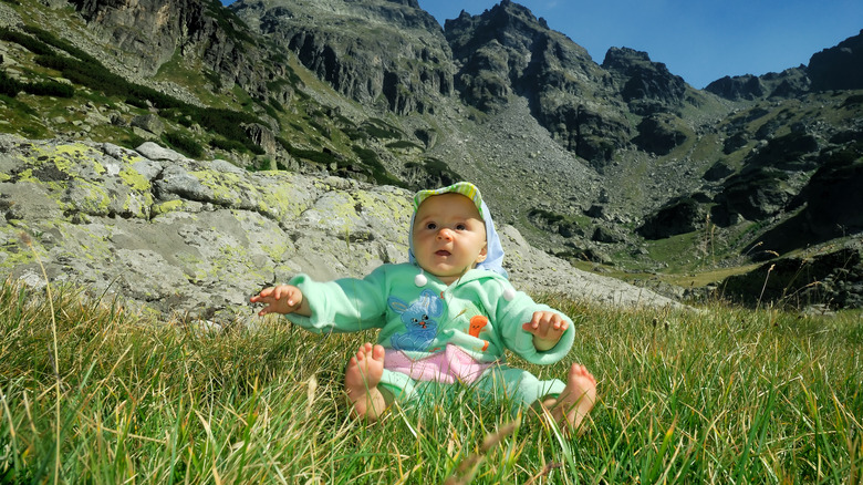 Baby sitting on grass in front of mountain ridge