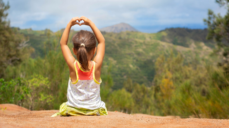 Little girl making heart with her hands in front of scenic vista