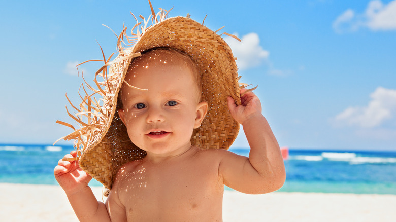 baby in a straw hat playing by the sea