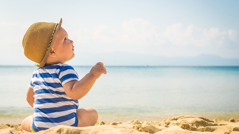 baby in a hat playing on the beach