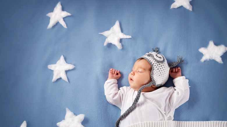 A sleeping baby wearing a bonnet lying on a blanket of stars