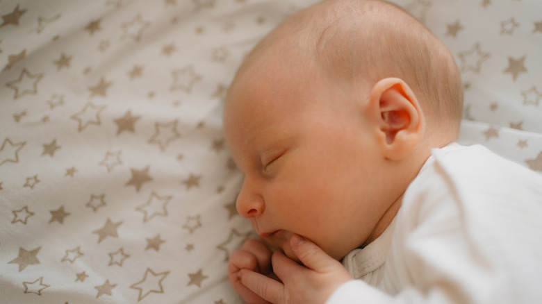 A baby sleeps on her side on a fitted sheet with stars