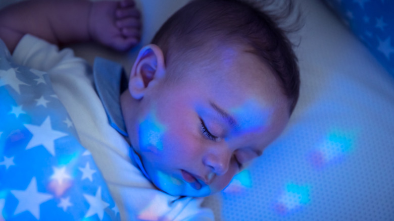 A baby sleeps with a star blanket and a nightlight casting stars on his face and all around