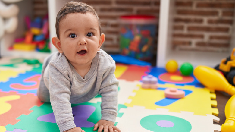 A baby boy crawls on all fours on top of a puzzle mat and play area