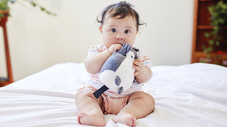 A little girl with curls sits on a bed while holding a stuffed bird