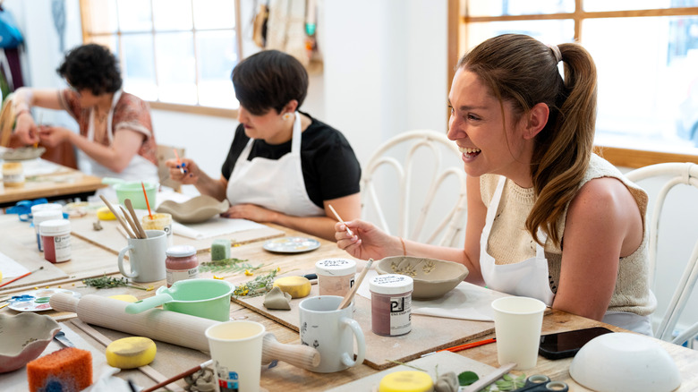 A mom-to-be laughs with friends while painting pottery together