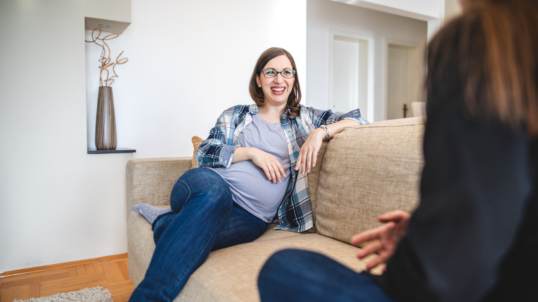 A pregnant woman laughs with a friend on the couch