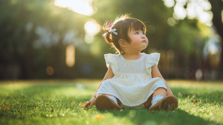 Baby girl sits in the grass with the sun setting behind her