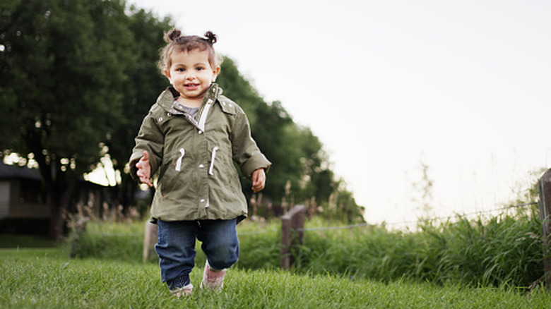 A toddler girl in a jacket plays outside at dusk