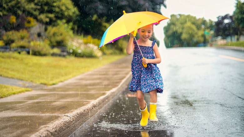 Young girl walks in rain wearing rainboots and holding an umbrella