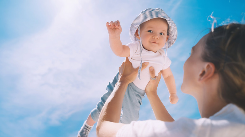 Mother holds up baby with a blue sky and white clouds in the background