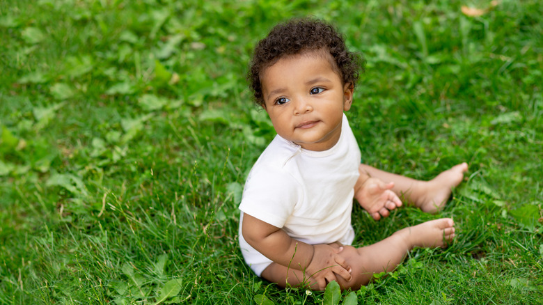 A baby sits in the grass