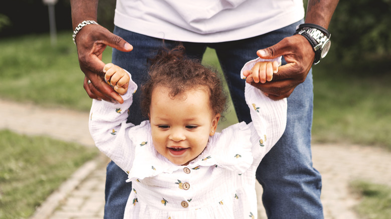 Toddler girl walking outside holding her father's hands