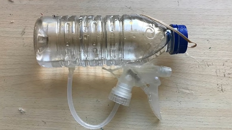 A plastic water bottle with a spray bottle sprayer connected to it to make a toy Super-Soaker