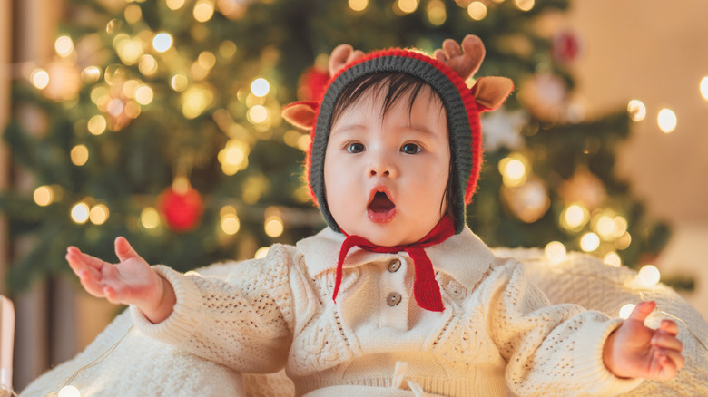 baby girl in front of a Christmas tree with a reindeer hat