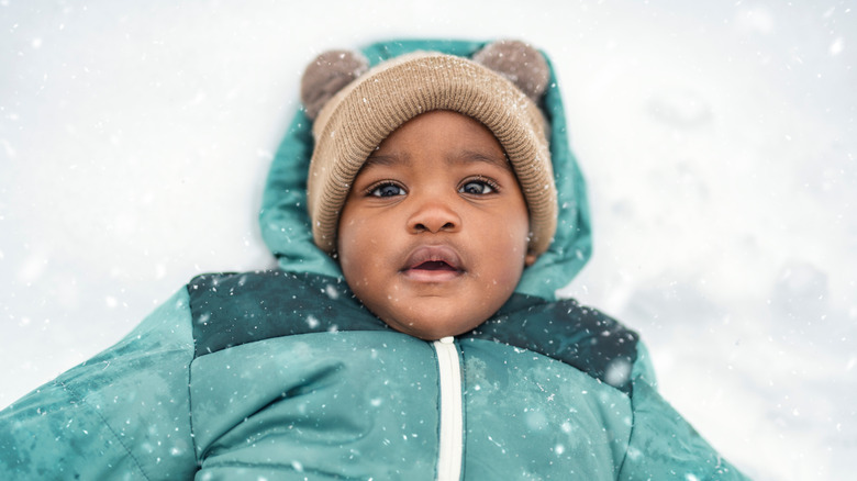 baby boy wearing a green jacket playing in snow