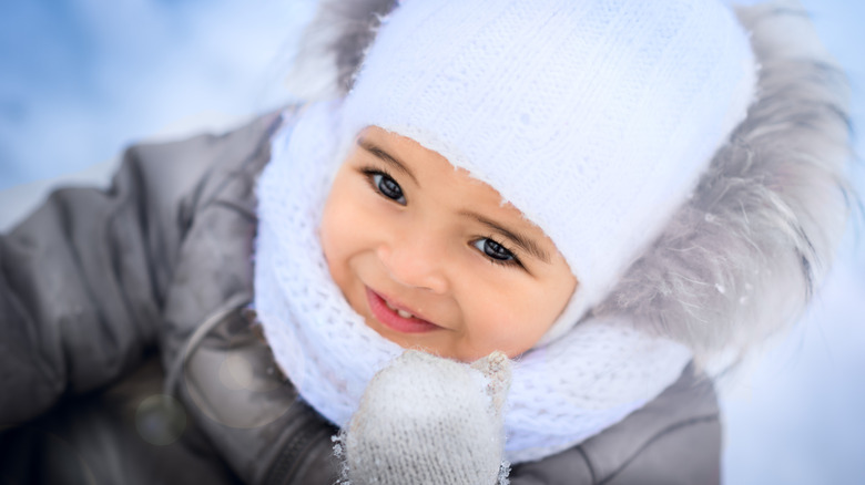 happy baby girl in winter wearing a white hat and gray coat