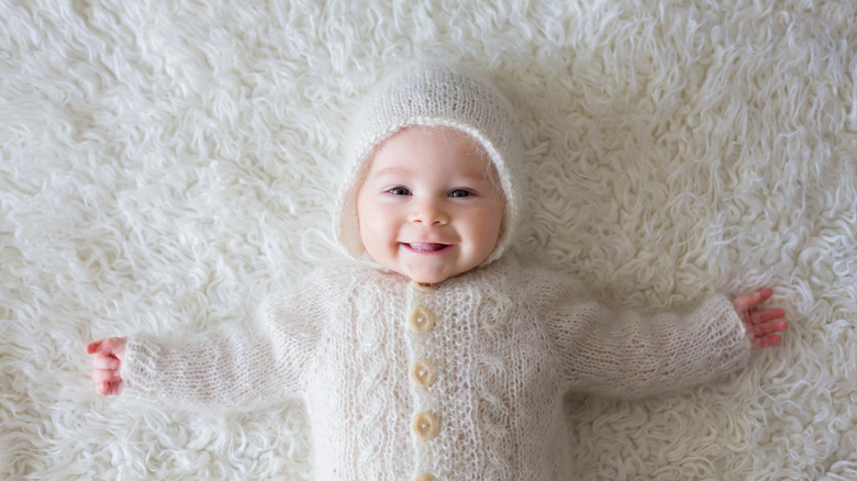 happy baby dressed in white winter clothes on a furry carpet
