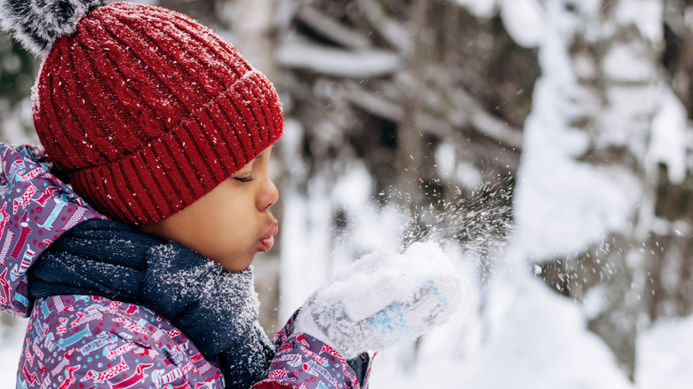 little girl blowing on a handful of snow