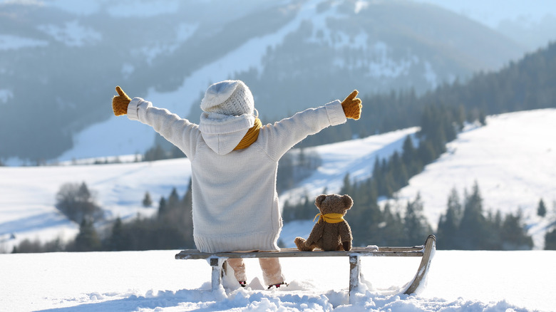 child happily sitting in the snow giving a thumbs up