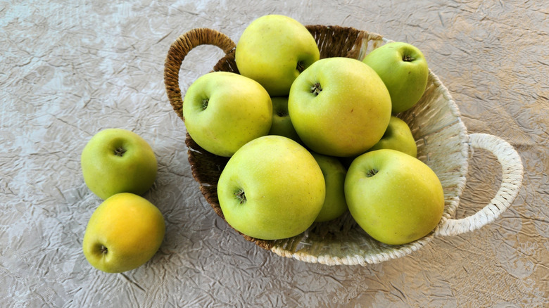 Top-down view of green apples in a woven bowl on a covered surface