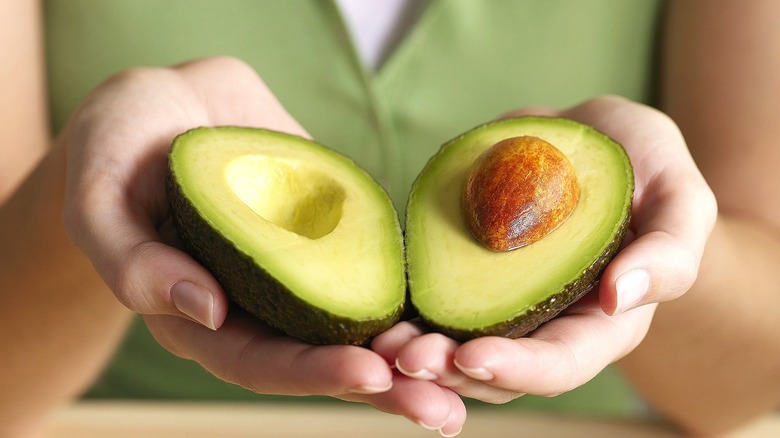 Close-up of two hands holding a halved avocado