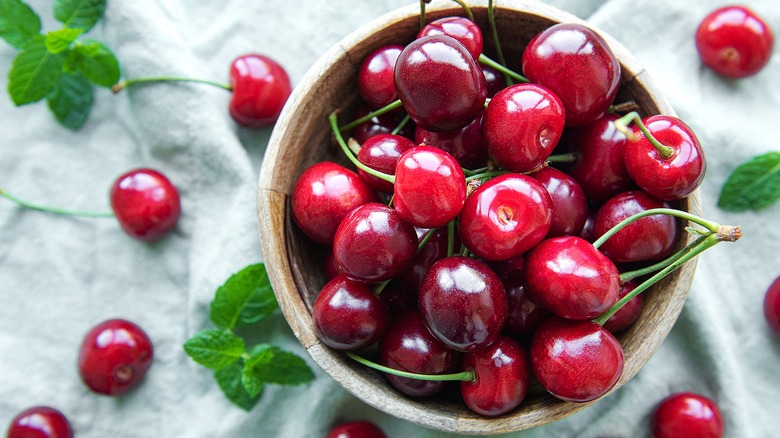 Top-down view of whole red cherries with stems in a cream-colored bowl