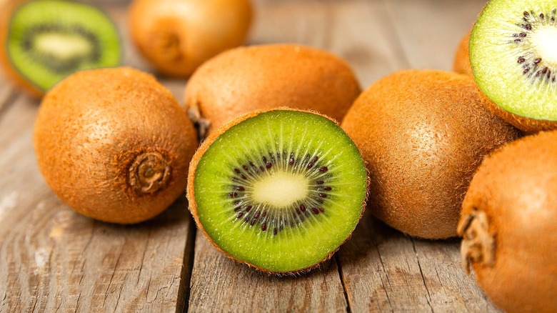 Whole and halved kiwi fruits on a slated wood surface