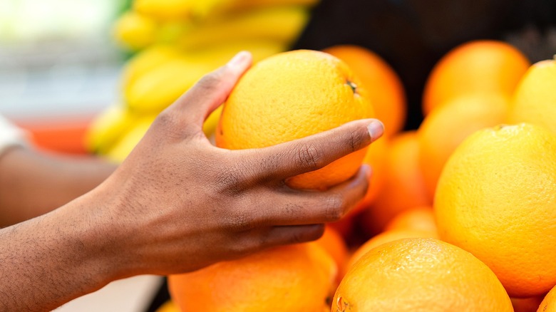 Hand holding an orange above other oranges