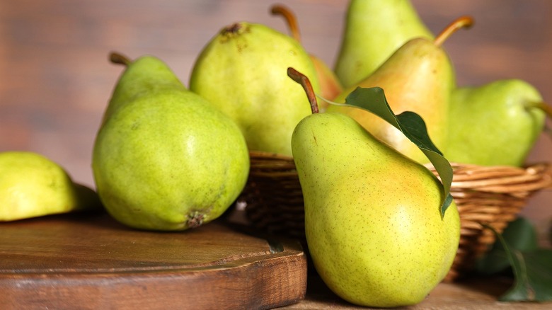 Whole green pears in a brown wicker basket and on a wood serving board
