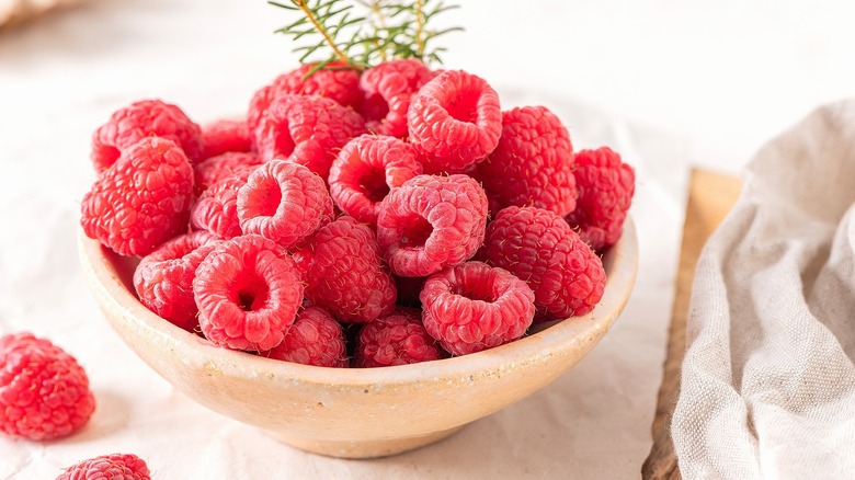 Fresh raspberries in a cream-colored bowl next to a cloth napkin