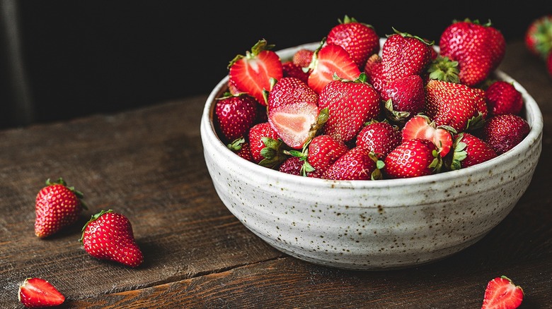 Fresh whole and halved strawberries in a speckled ceramic bowl on a dark wooden table